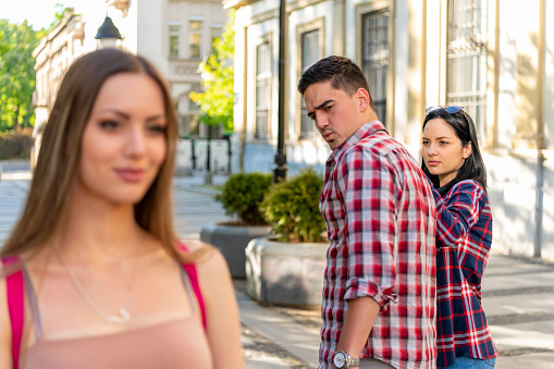 Disloyal man walking with his girlfriend and looking amazed at another seductive girl