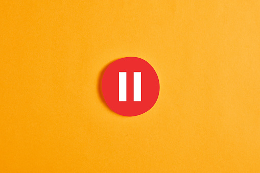 Red round circle with a pause button or icon against yellow background.