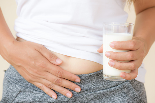 Woman hand holding glass of milk having bad stomach ache because of Lactose intolerance. health problem with dairy food products, Healthcare and medical concept.